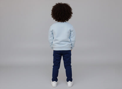 Child wearing a light blue sweatshirt and dark blue pants on a plain background