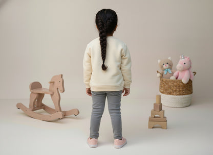 A girl standing with a wooden rocking horse and a basket of toys on a plain background