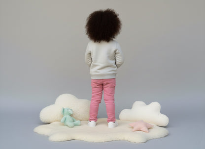A girl standing on a cloud-shaped rug with toys on a plain background