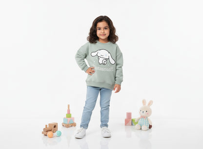 Girl wearing a Mint green sweatshirt with a Cinnamoroll design, standing on a white background with toys around.