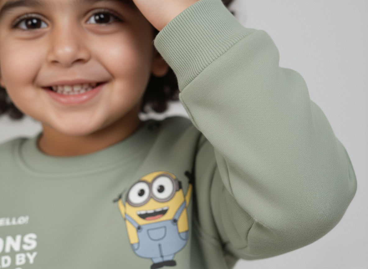 Child wearing a mint green sweatshirt with minion cartoon character, smiling.