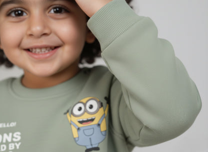 Child wearing a mint green sweatshirt with minion cartoon character, smiling.