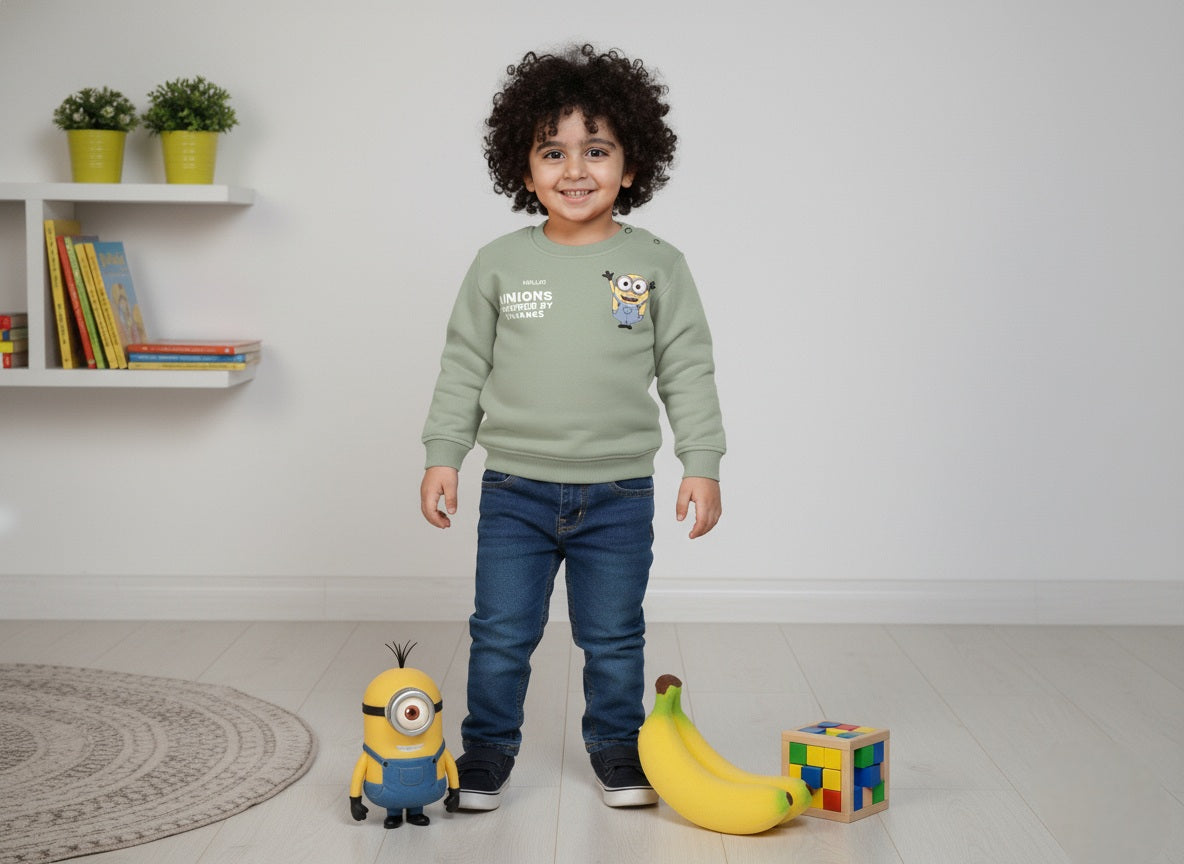 A child wearing a mint green sweatshirt with Minions cartoon character, standing in a room with toys and plants.