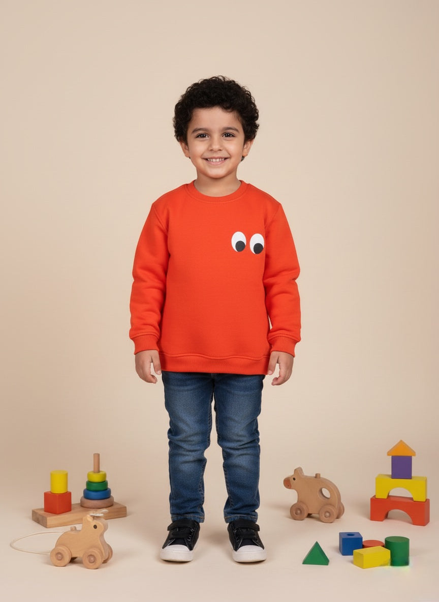 Child wearing an orange sweatshirt with a face design, standing in front of colorful wooden toys on a beige background