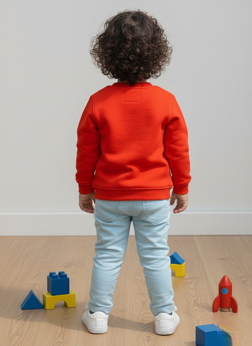 Child wearing an orange sweatshirt and light blue jeans standing on a wooden floor with colorful building blocks.