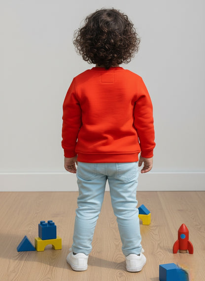 Child wearing an orange sweatshirt and light blue jeans standing on a wooden floor with colorful building blocks.