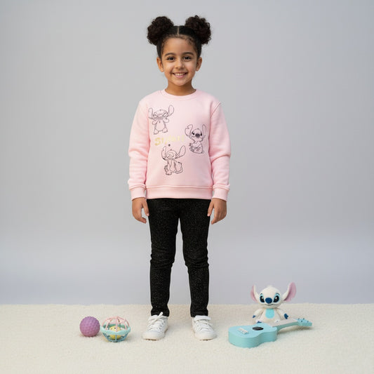 Child wearing a pink sweater with stitch cartoon character designs, standing on a light gray background with toys around.